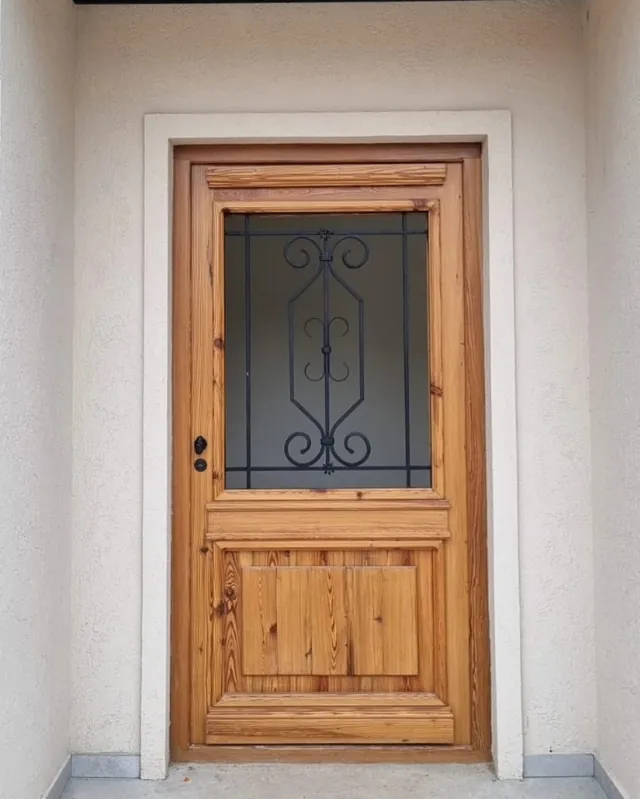 Puerta colonial de una hoja con reja en un frente blanco